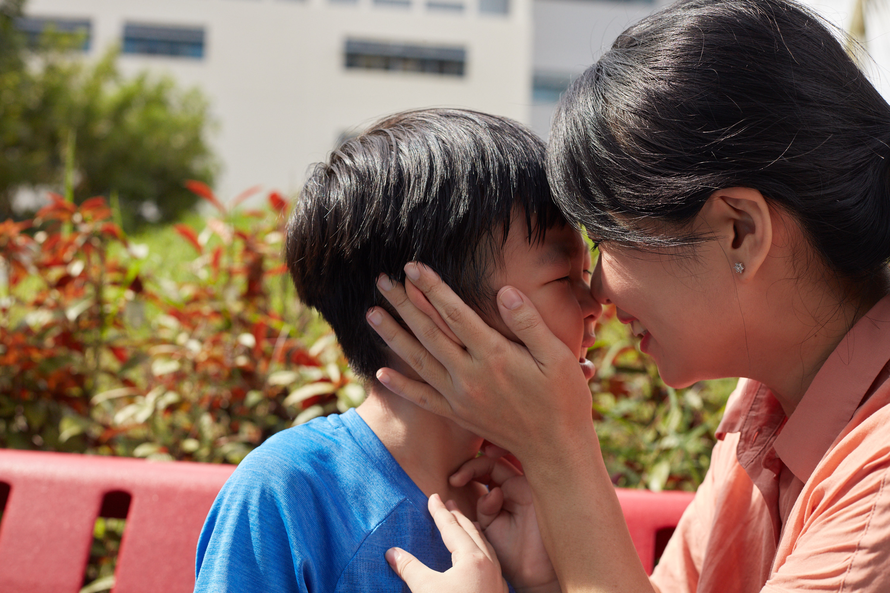 A mother holding her son's face close to hers, both smiling widely.