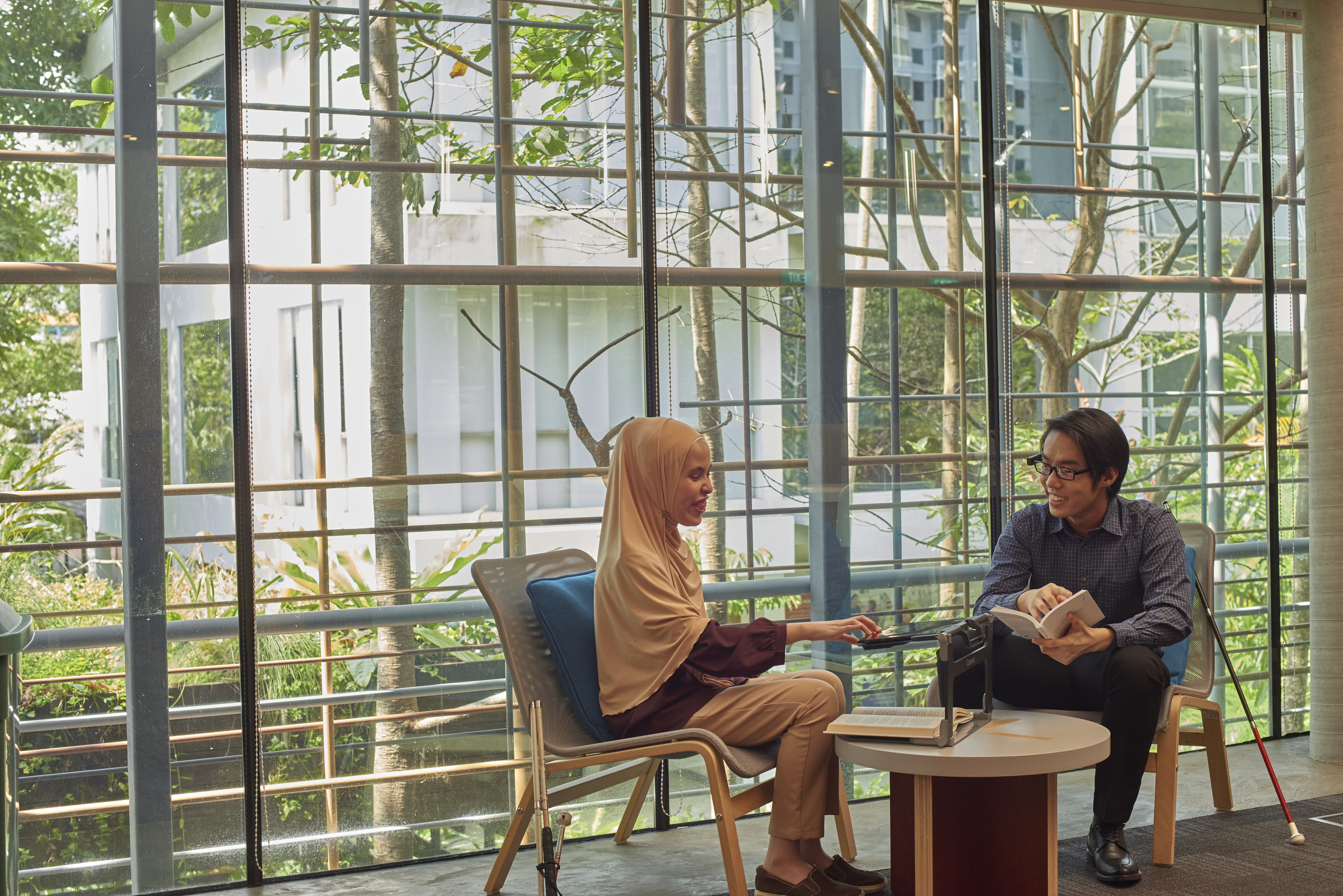 A Malay lady with a Chinese man in an office setting, using assistive tech devices.