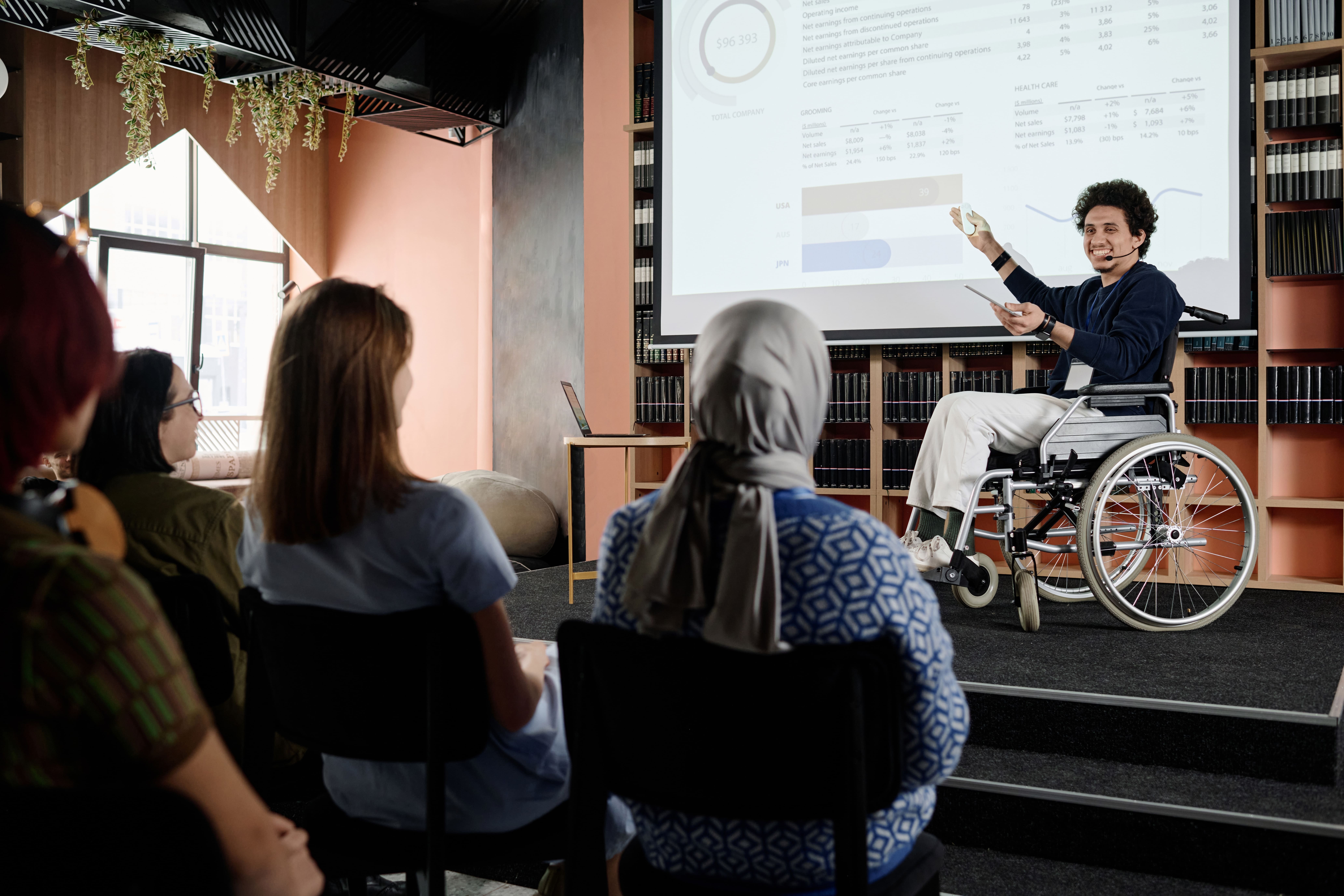 A man who uses a wheelchair giving a presentation to a seated audience.