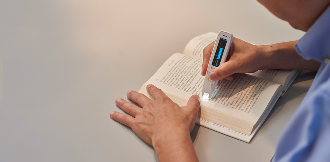 A man uses the Reader Pen (C-PEN®) to scan each line in a book to read the content.