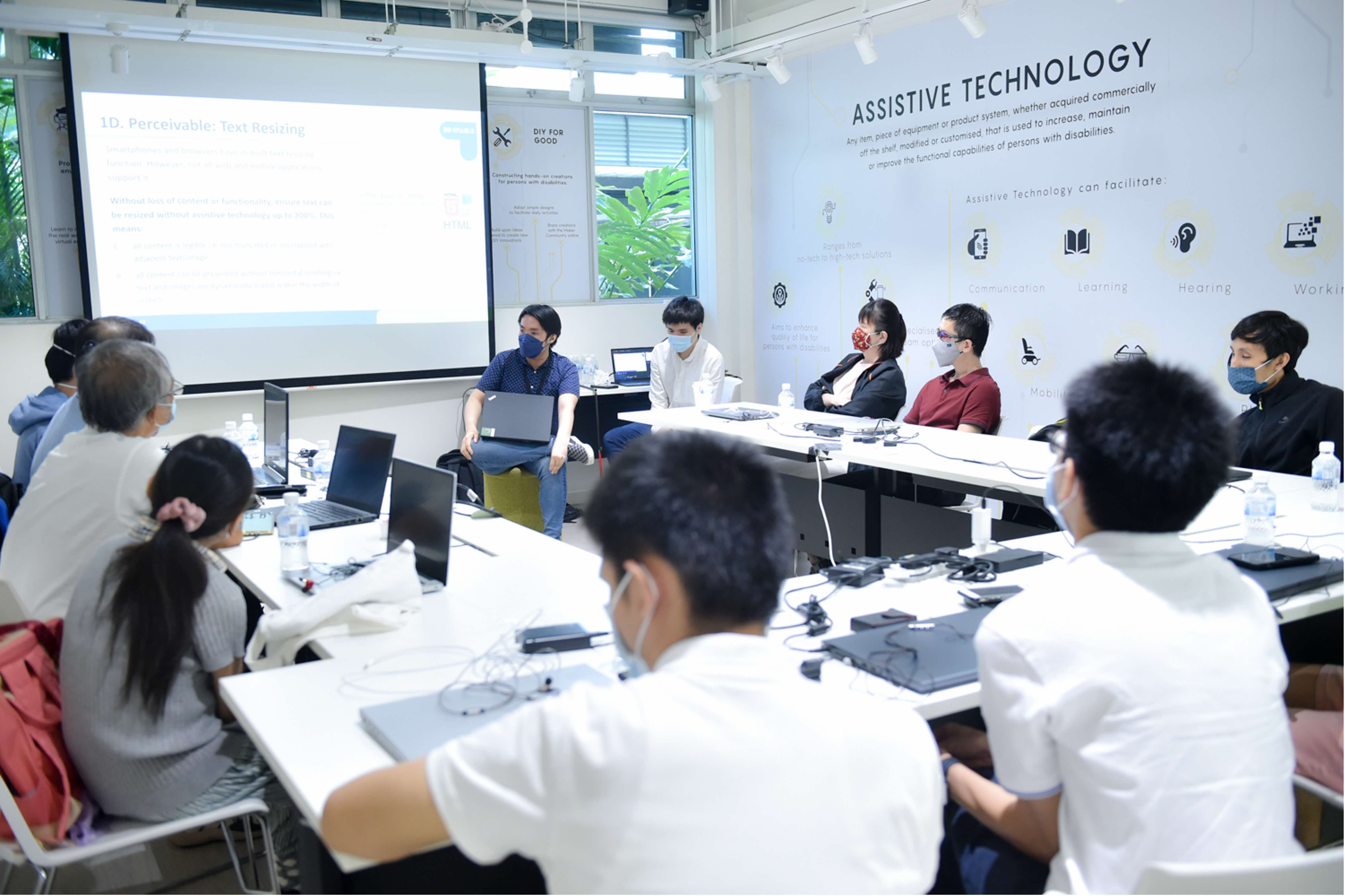 E-accessibility workshop at Tech Able. A trainer sits at the front of the class, surrounded by participants with their laptops in front of them.