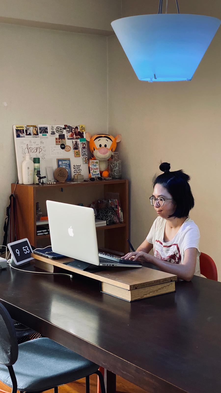 Isabelle, who is deaf, using her laptop with a google nest next to her, and a smart lamp above her. The lamp changes colour accordingly. Photo credit: The Straits Times