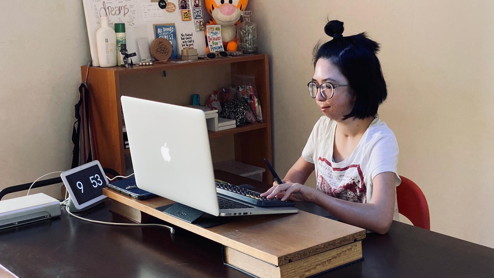 Isabelle, who is deaf, using her laptop with a google nest next to her, and a smart lamp above her. The lamp changes colour accordingly. Photo credit: The Straits Times