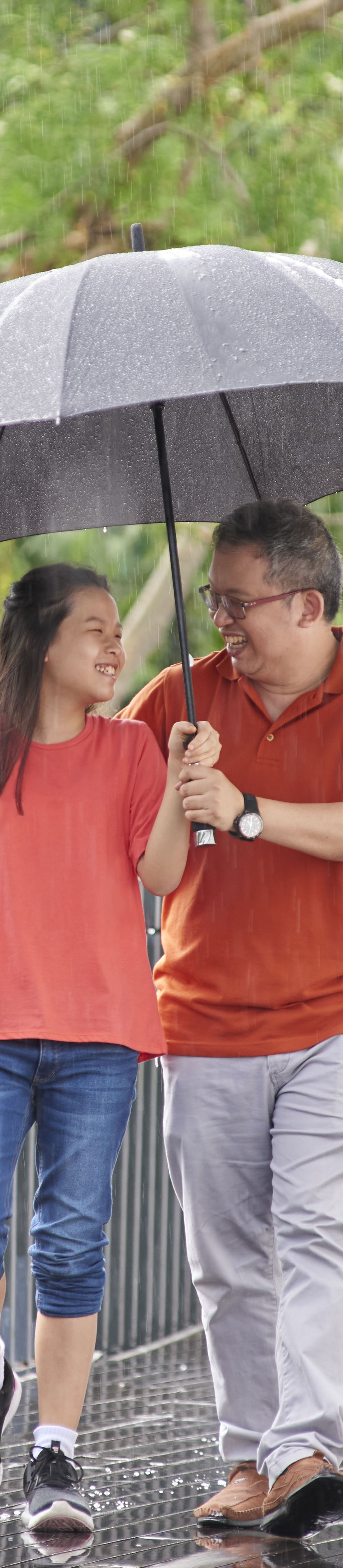 Father sheltering his daughter with an umbrella while walking in the rain.