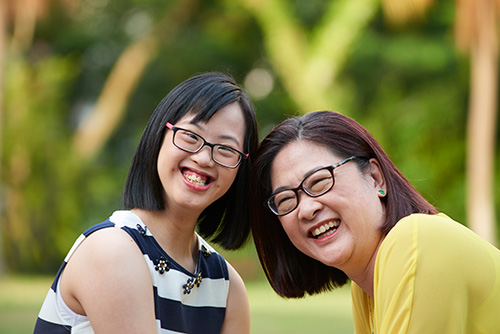 An image of a caregiver with her child with down syndrome smiling at the camera