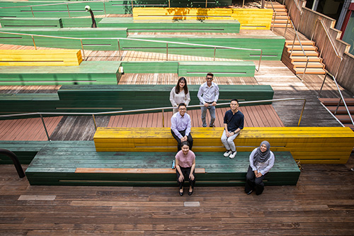 A group of people seated at a terrace, looking up and smiling at the camera