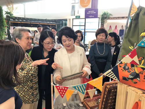 Korea's First Lady admiring a pouch at The Art Faculty during her visit to Enabling Village. Mdm Ho Ching (wife of PM Lee) explains about The Animal Project while standing next to her.