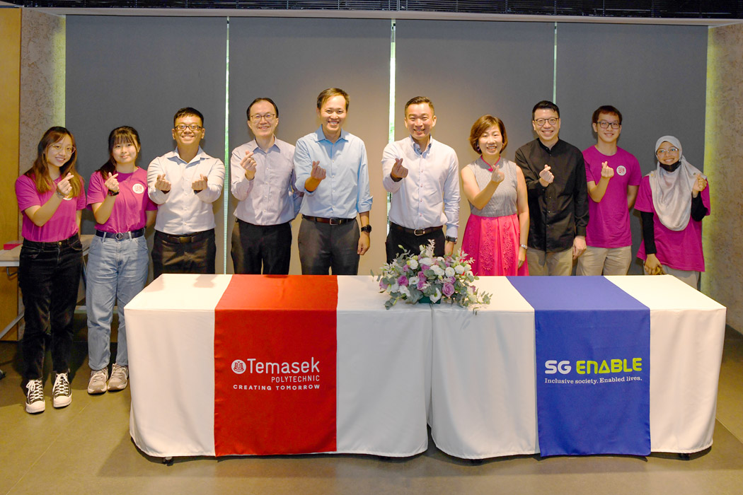 Group photo taken during the MOU signing between Temasek Polytechnic and SG Enable. Features SG Enable and Temasek Polytechnic's CEOs as well as student volunteers. Everyone is posing with finger hearts.