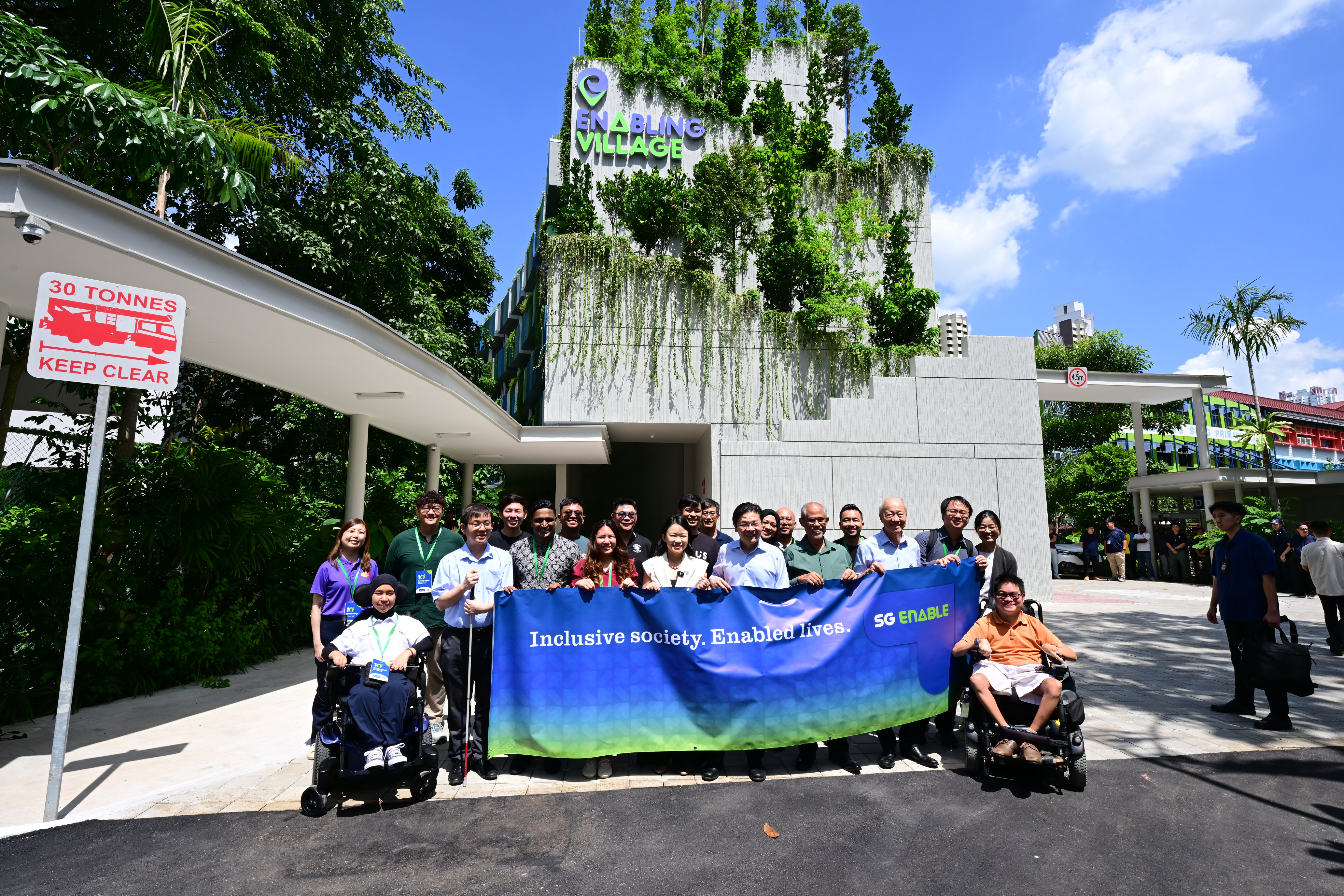 A group of people including PM Lawrence Wong holding up SG Enable's banner in front of the Vista building in Enabling Village.