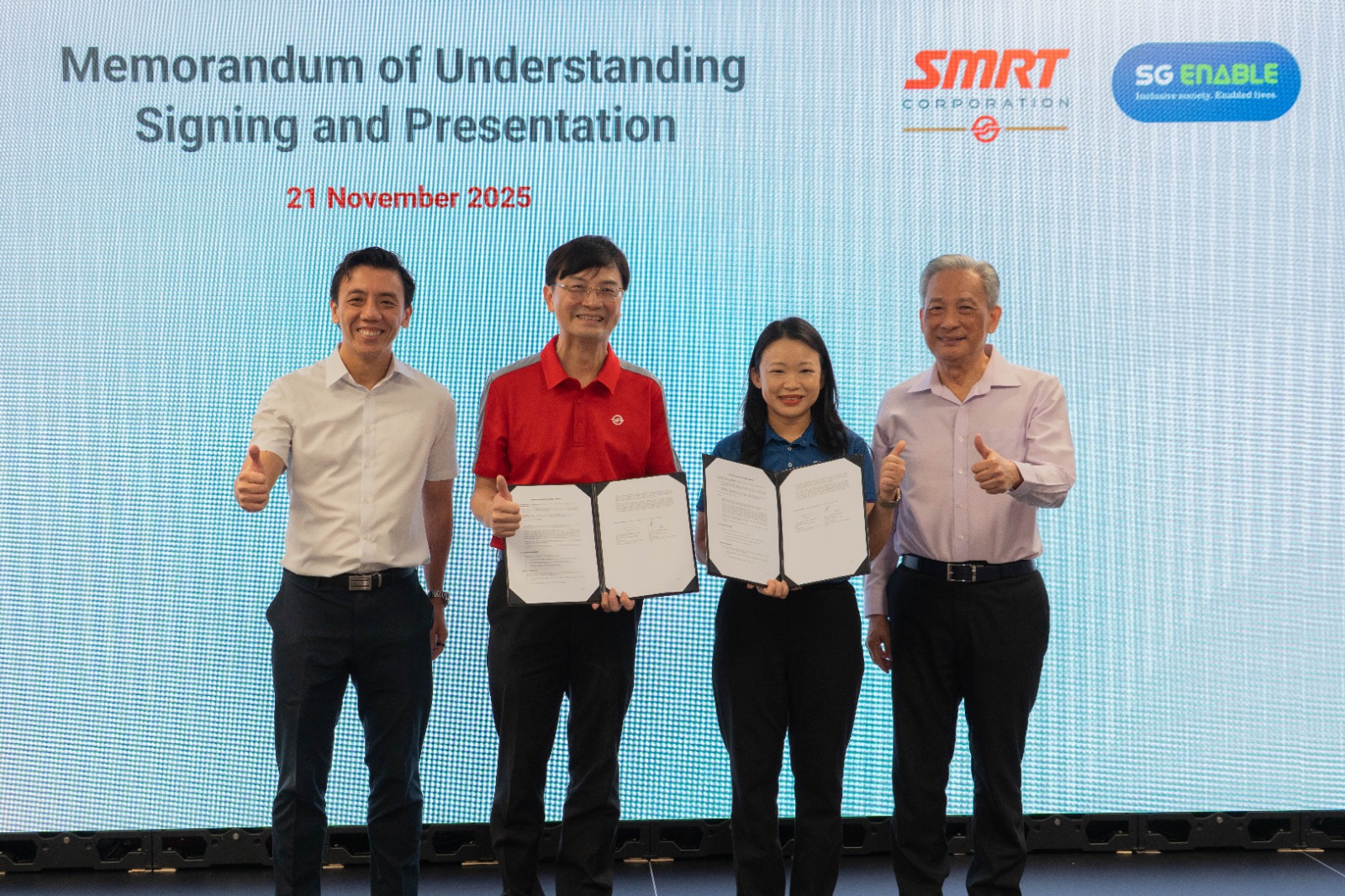 A group of 4 people standing on stage holding up two signed documents.
