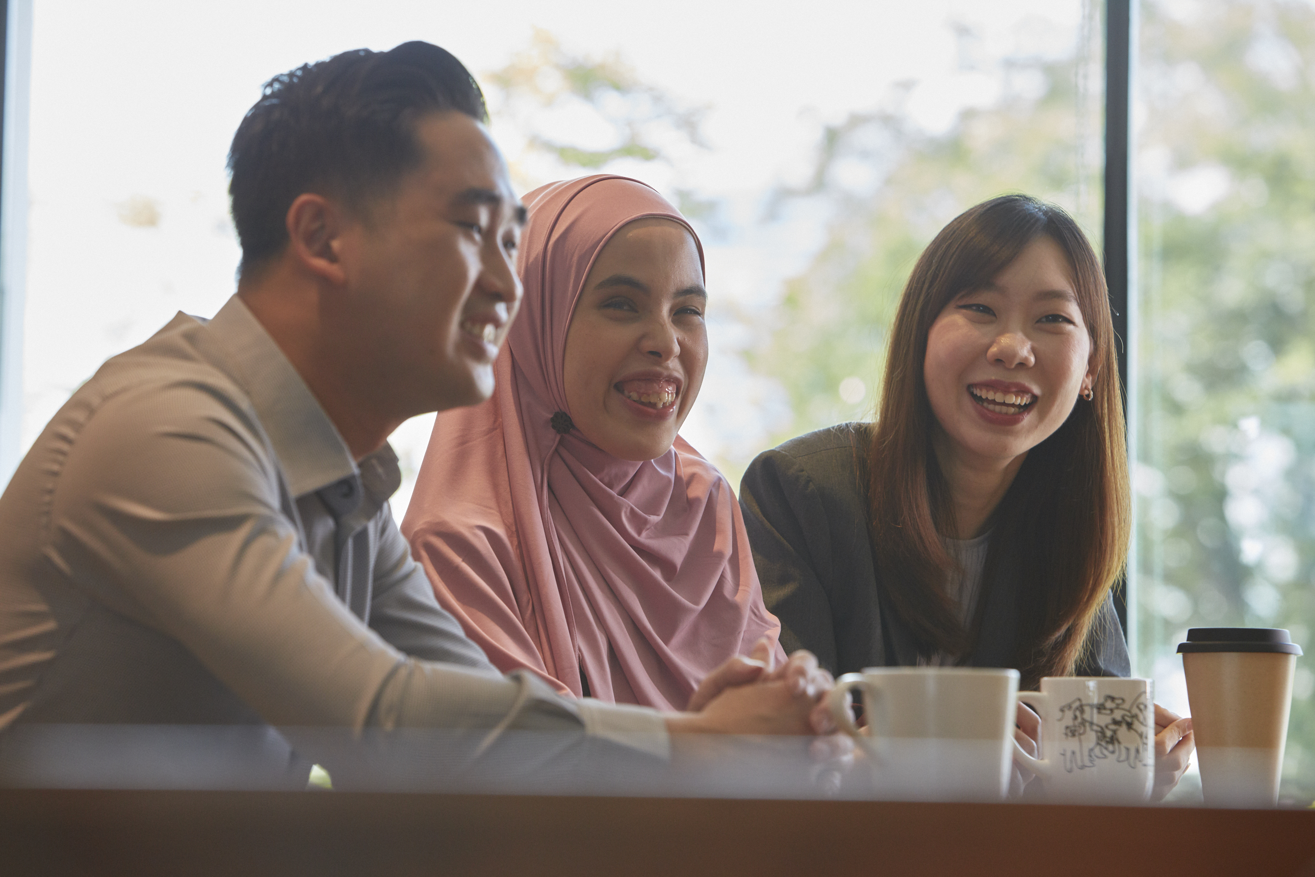 In an office pantry setting, three colleagues interact with one another.