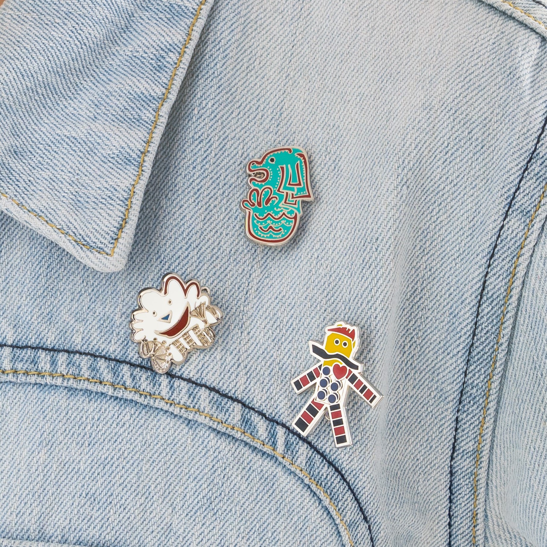 Three enamel pins on a light denim jacket