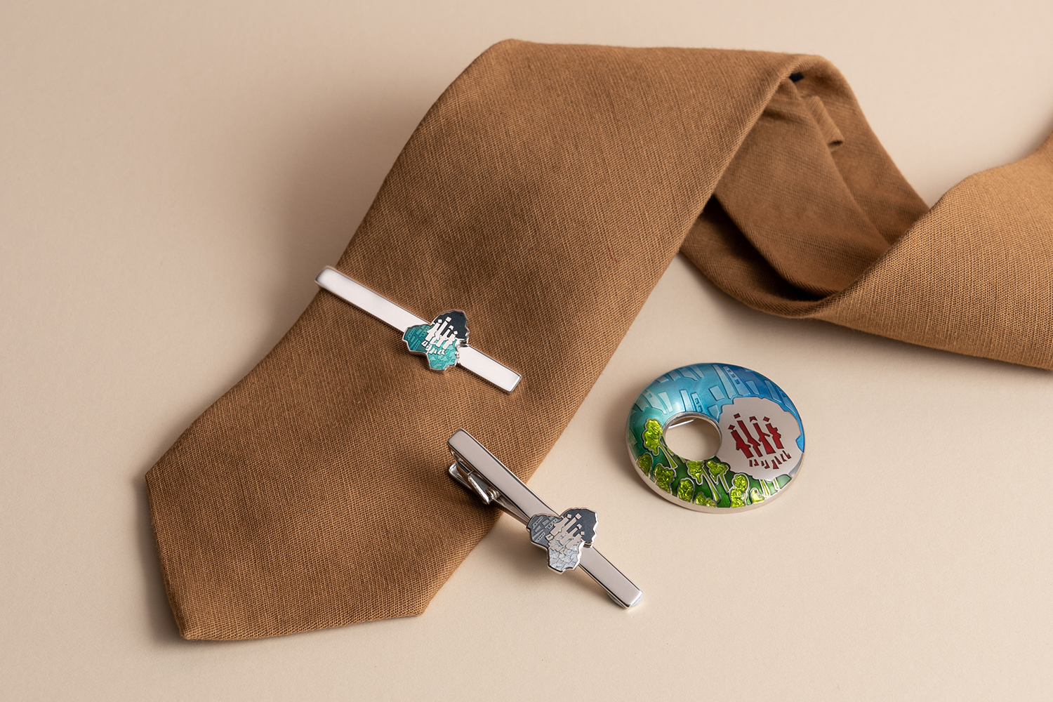 A brown tie in the background, with 2 tie clips and a brooch in the foreground.