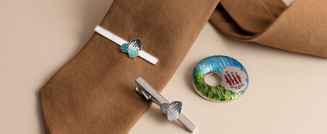 A brown tie in the background, with 2 tie clips and a brooch in the foreground.