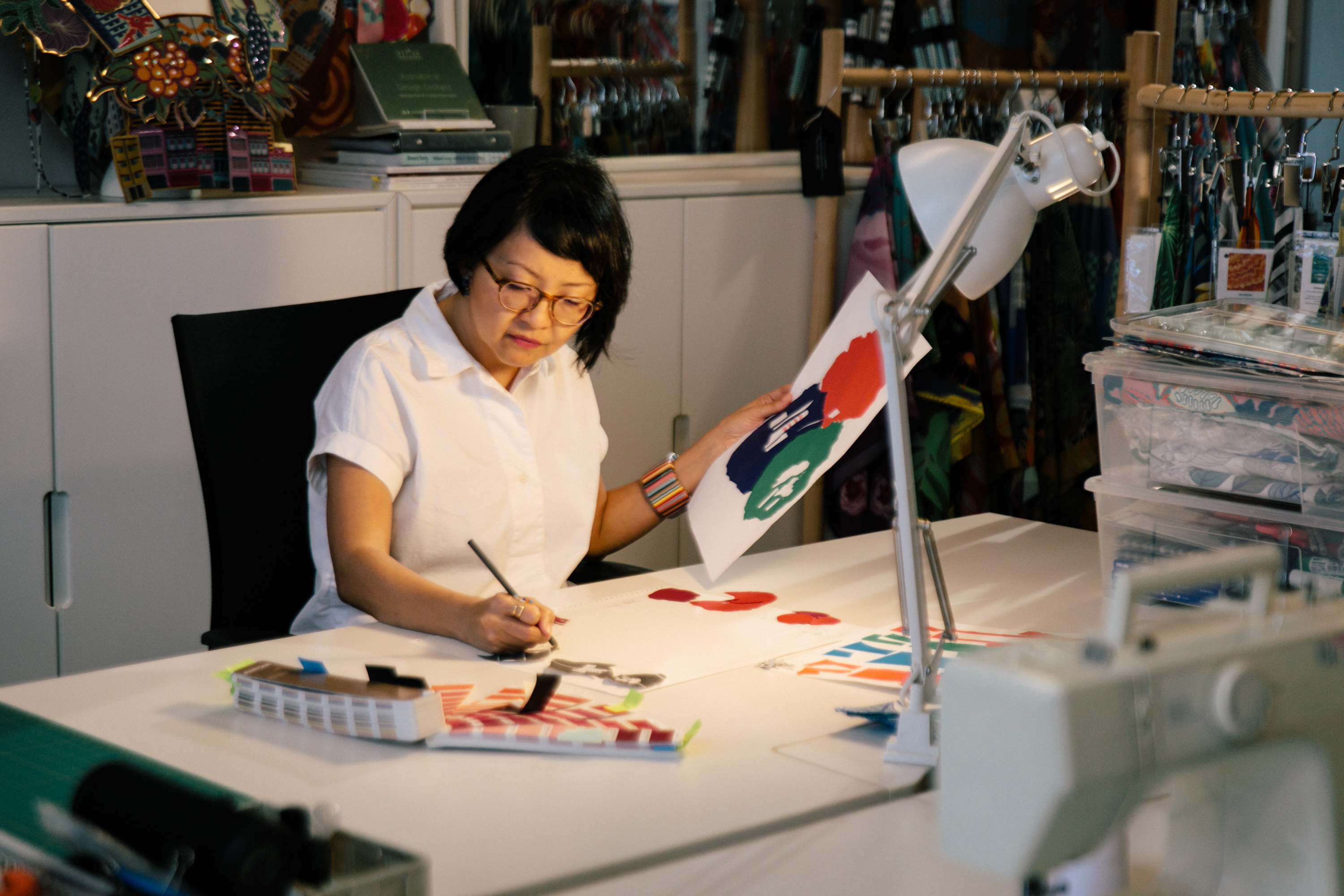 A lady sketching with one hand, and holding a reference picture in the other.