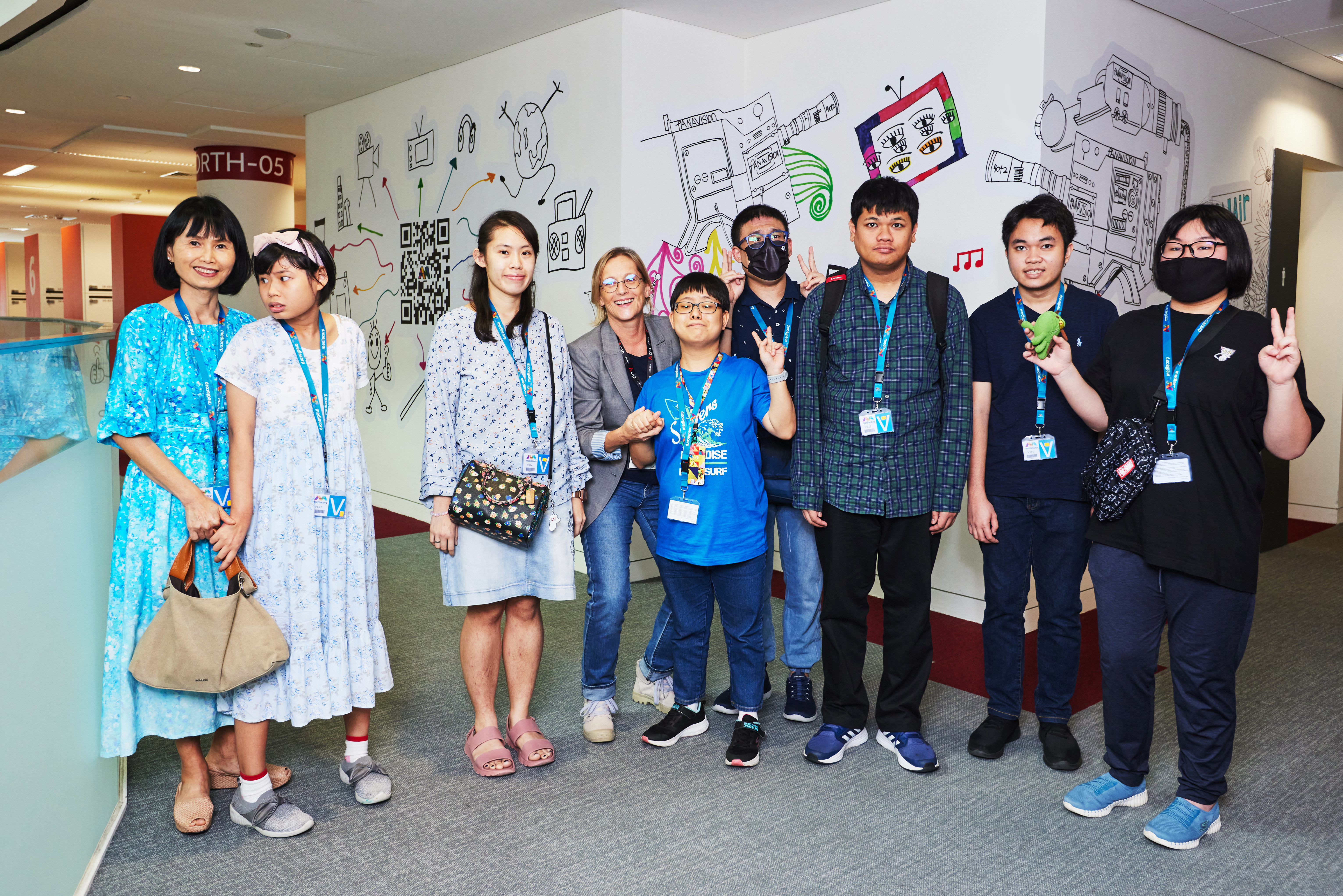 Artist with disabilities cheerfully posing next to each other in front of a wall mural at Mediacorp Campus