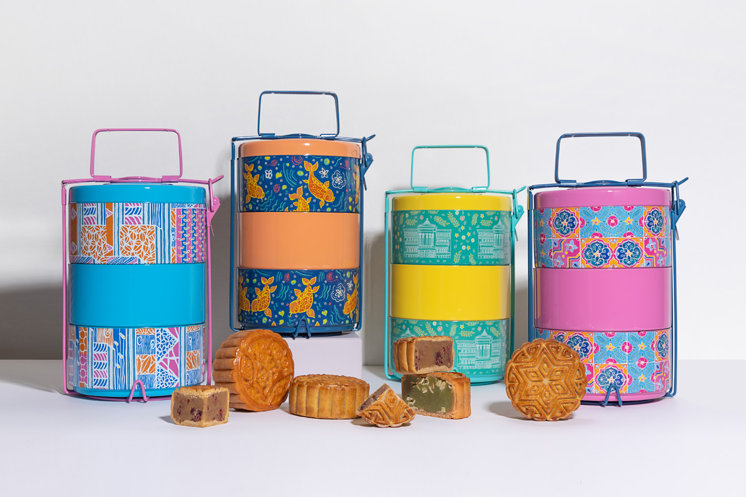 A collection of 3-tier tiffin carriers with colourful prints, a few mooncakes are on display in front of them.
