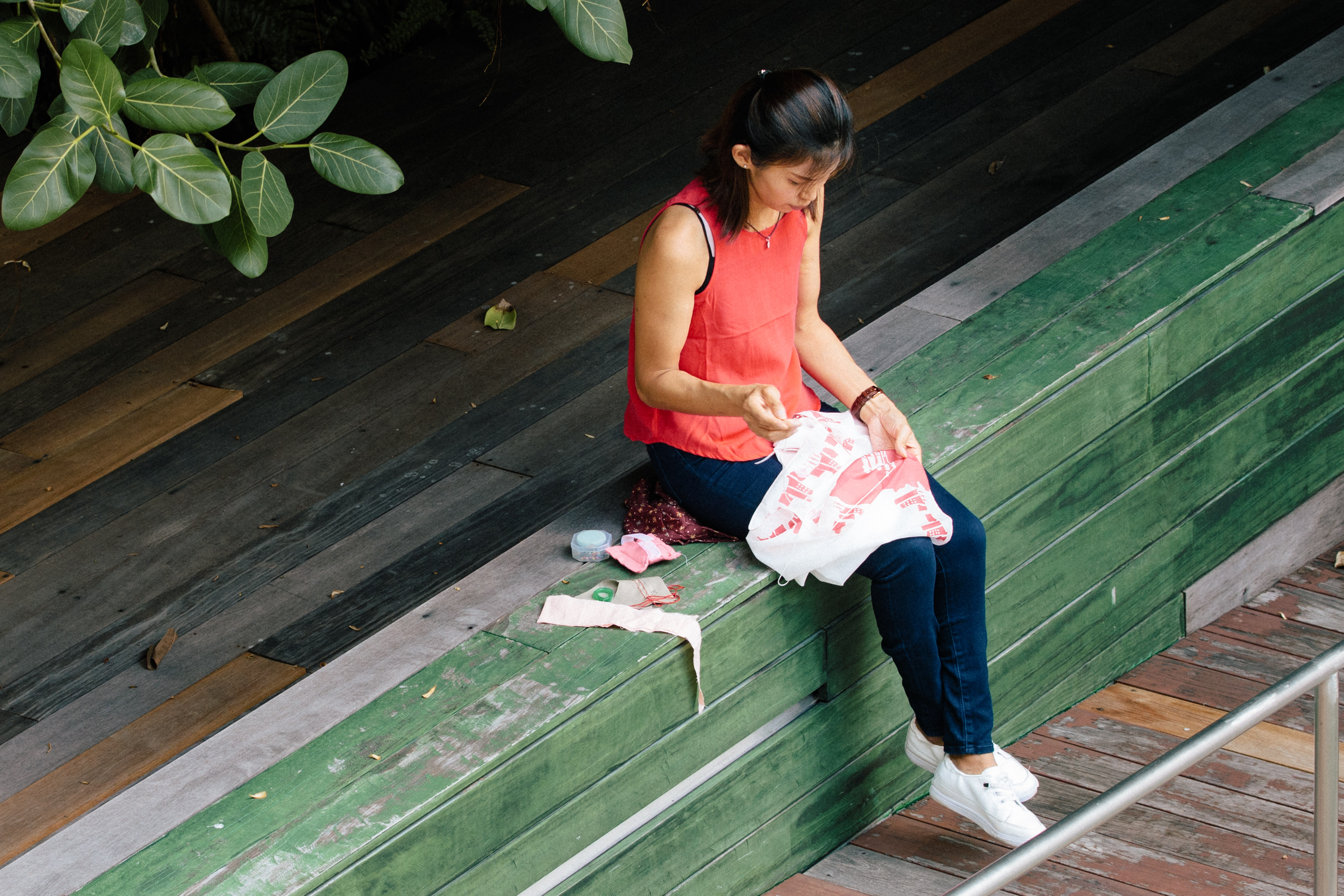 A lady in red sitting on a bench, working on her embroidery. 