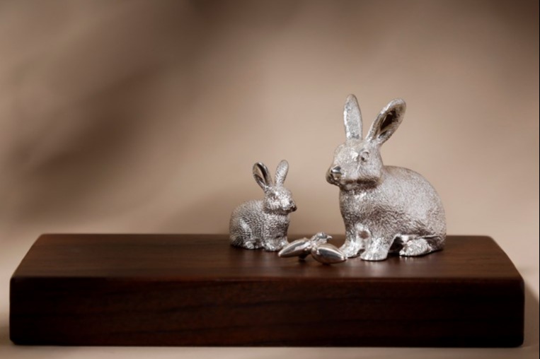 An ornament of two rabbits and two radishes made out of silver on a wooden base.