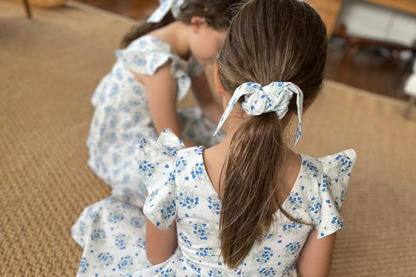 Two young girls wearing white dresses with prints of bouquets of blue hearts, and matching hair ties.