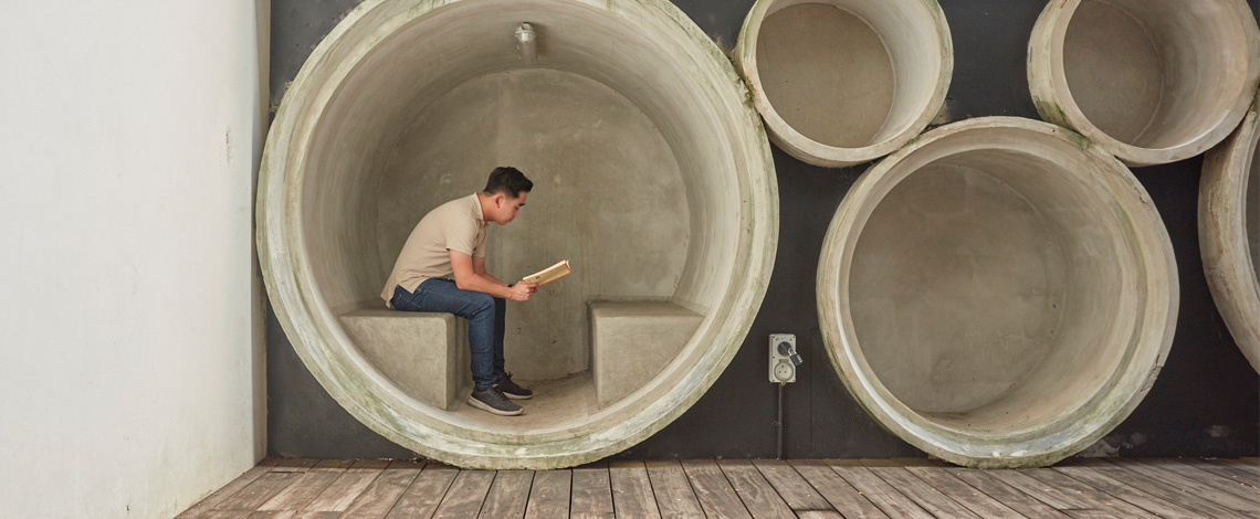 A man is seated and reading in cylindrical-looking rest area