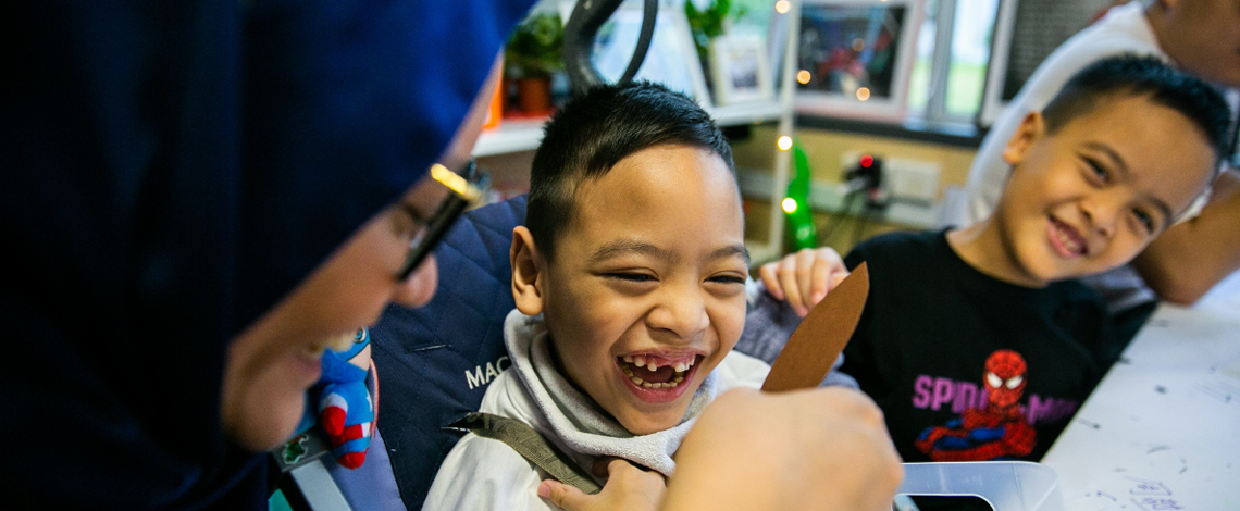 Photo banner of a caregiver and her son smiling while creating an artwork