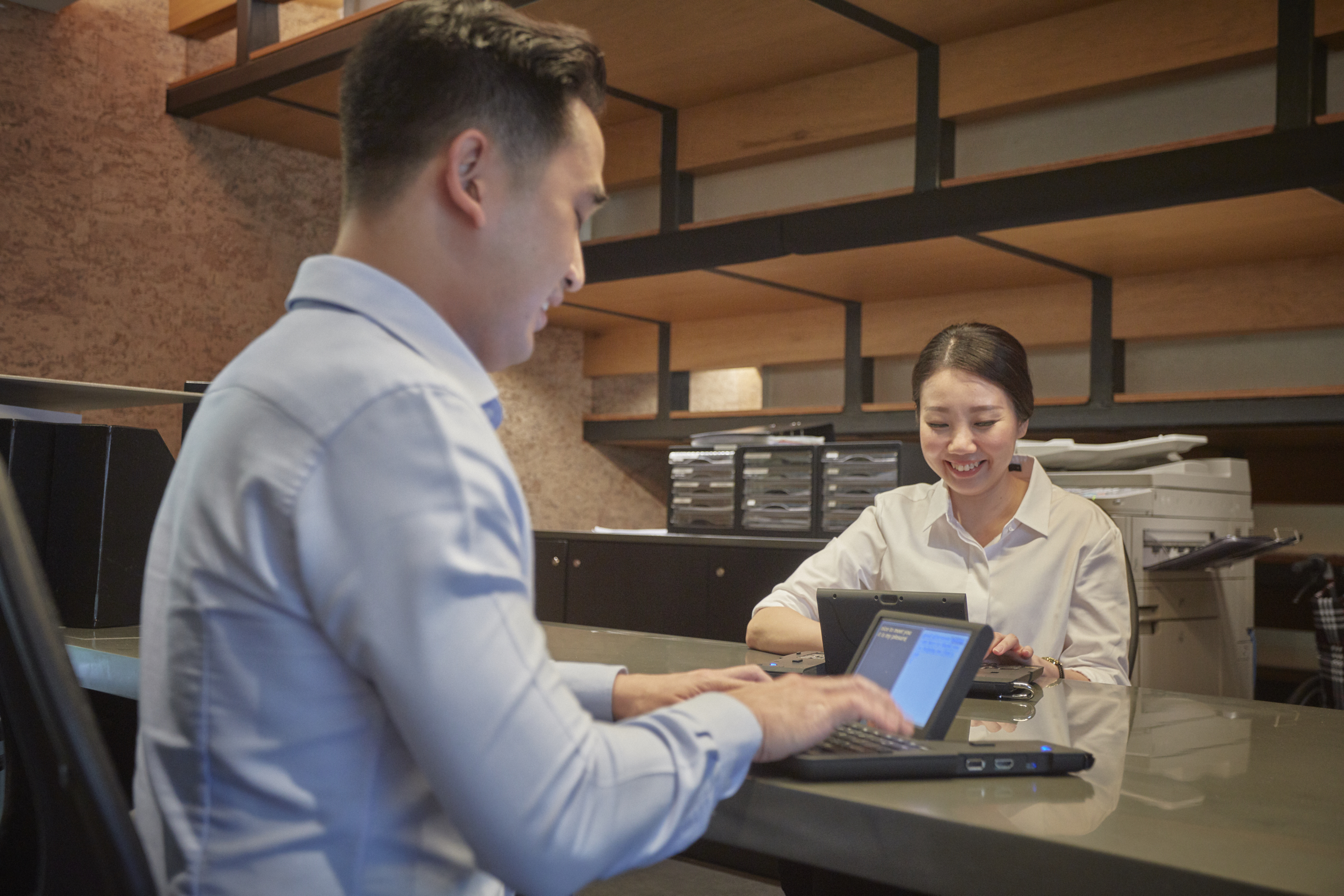 Two people seated at opposite sides of a counter, meeting and looking at their mobile devices.