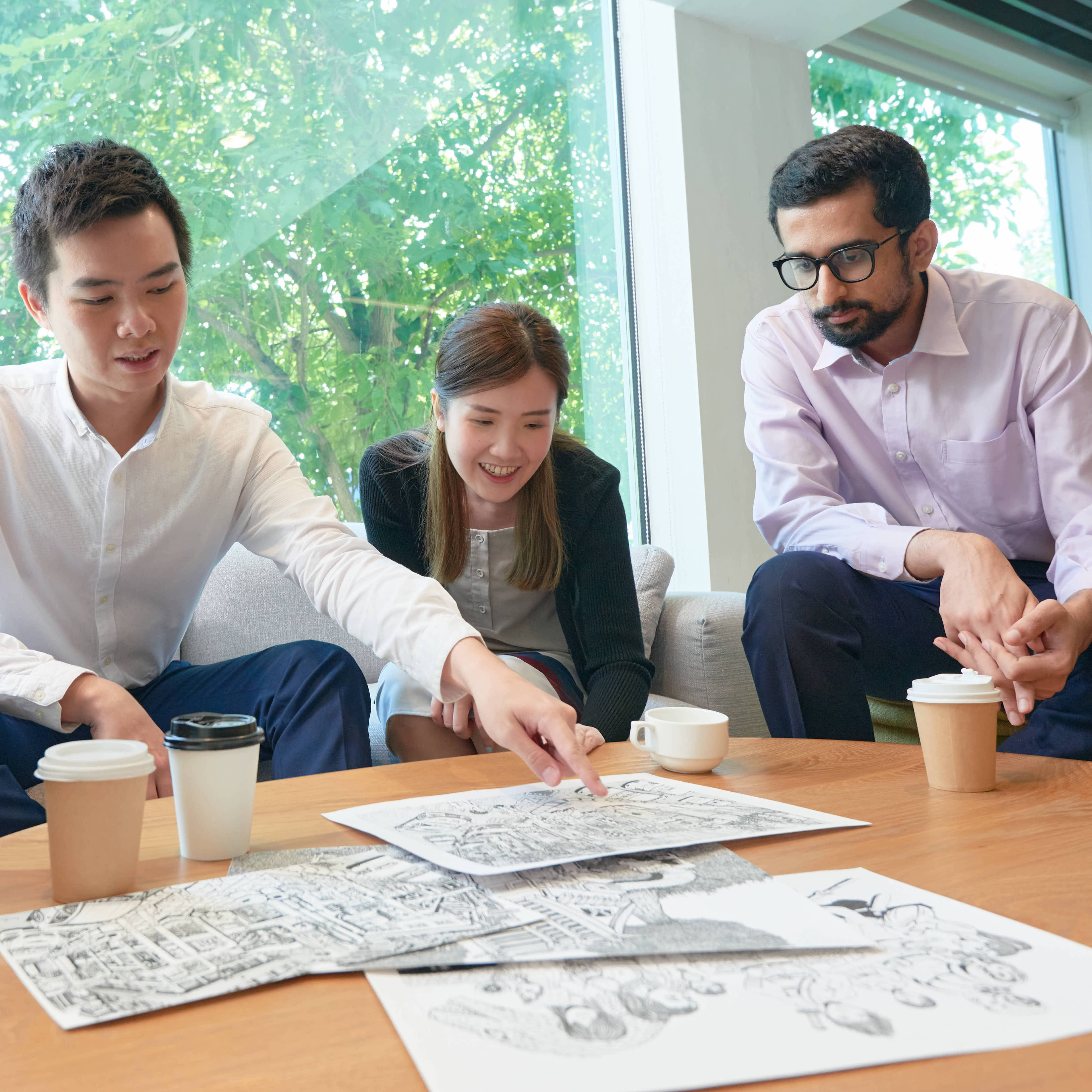 Four professionals looking at illustrations on papers on a table in front of them, as one professional points to the papers.