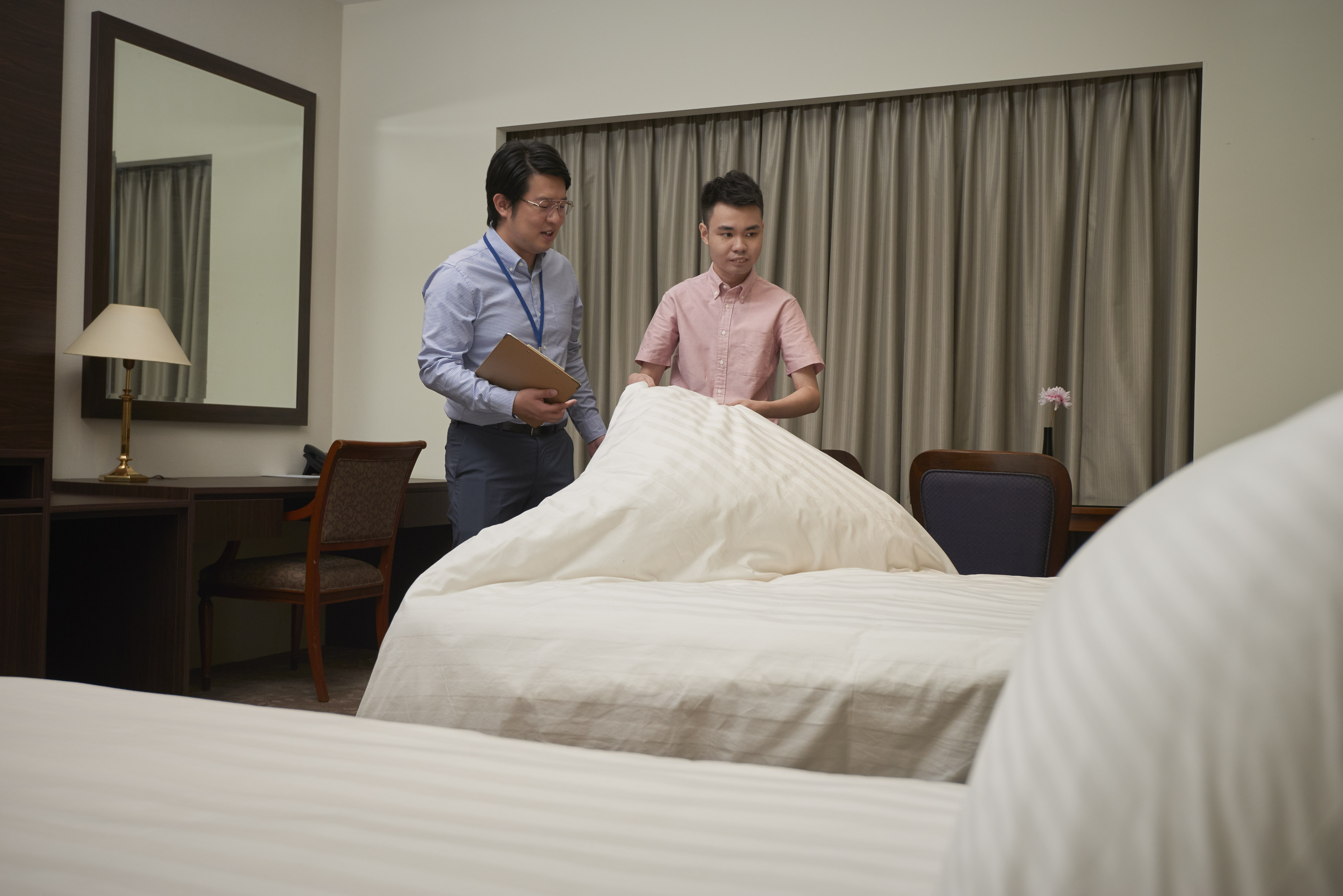 A professional guiding a person with disability in housekeeping duties such as neatly making beds.