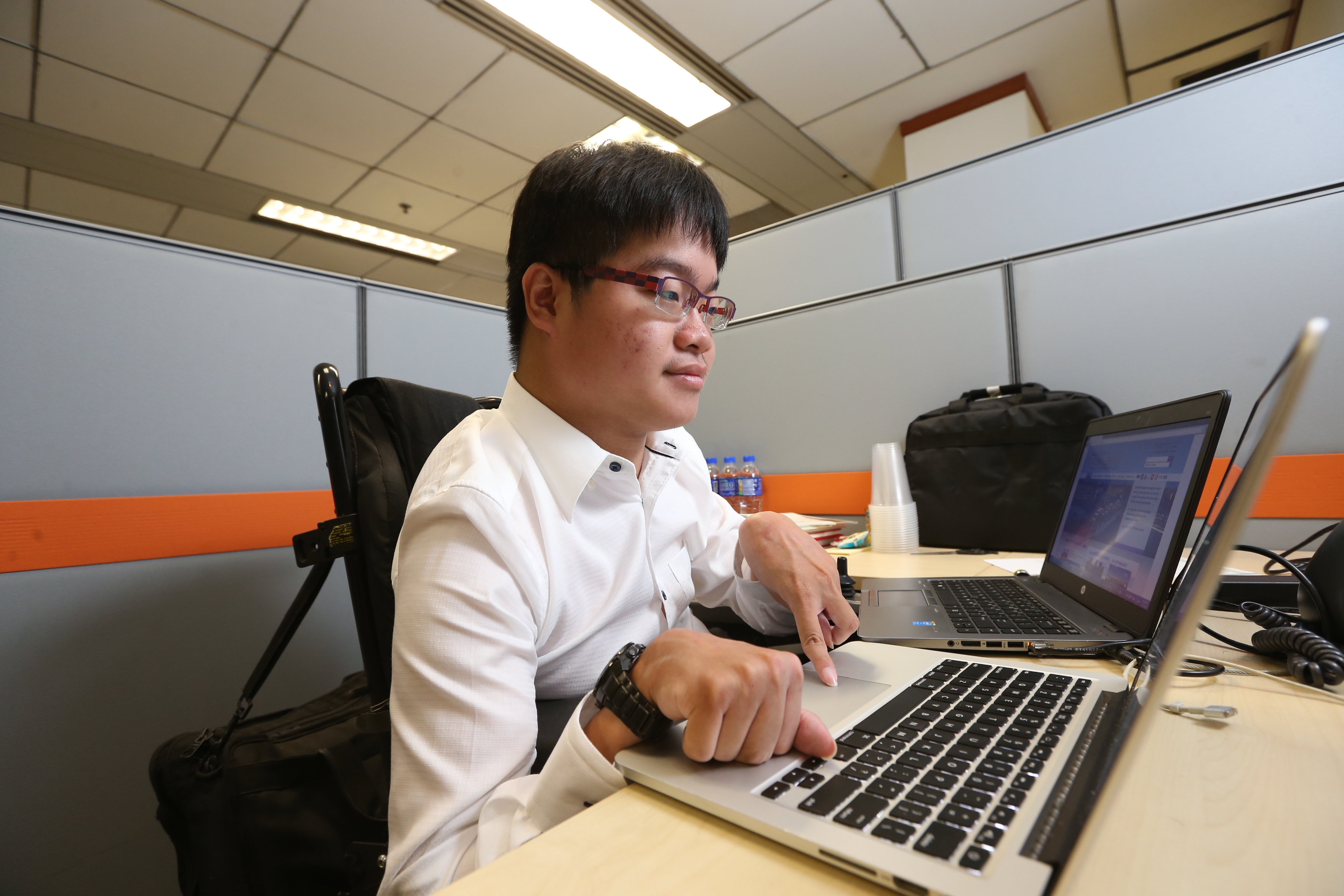 A wheelchair user using two laptops on a work desk.