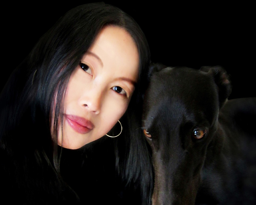 A woman with long black hair is pictured next to a black dog.
