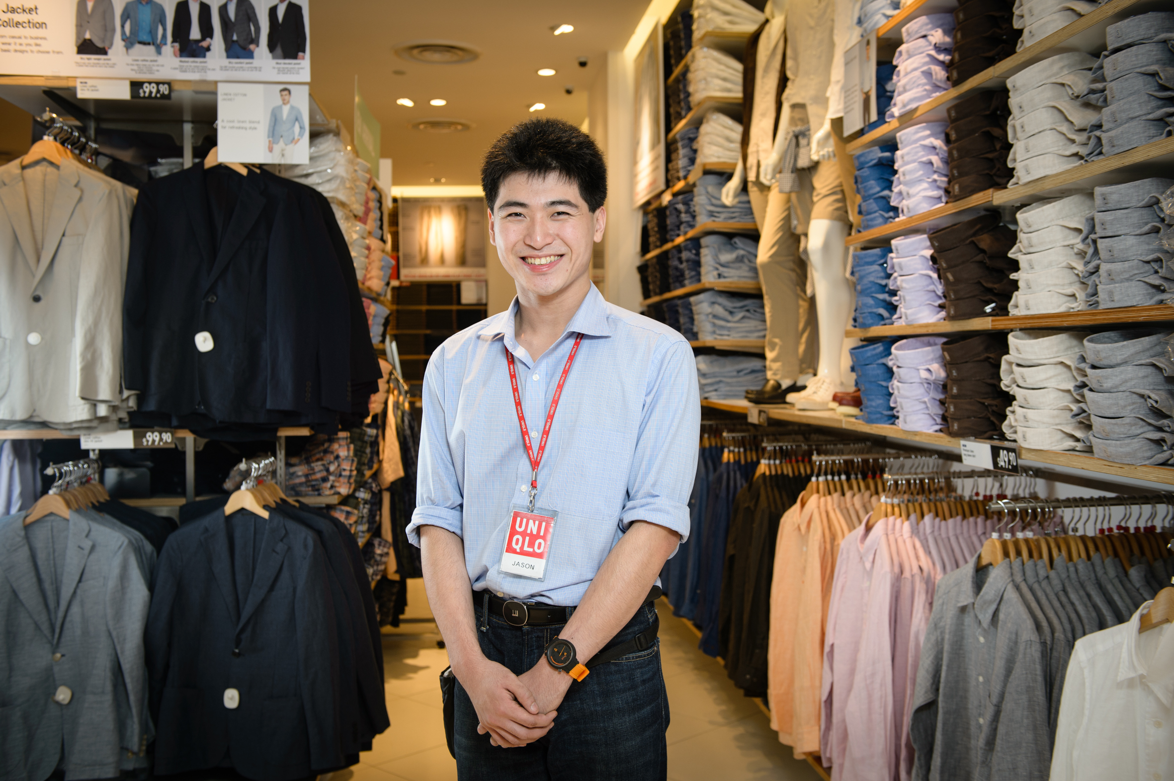 A man wearing a Uniqlo lanyard smiles for the camera; surrounding him are various fashion apparel.