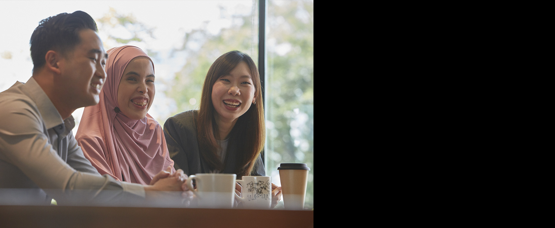 Three professionals, including a woman with visual impairment, seated at a table with drinks and smiling.