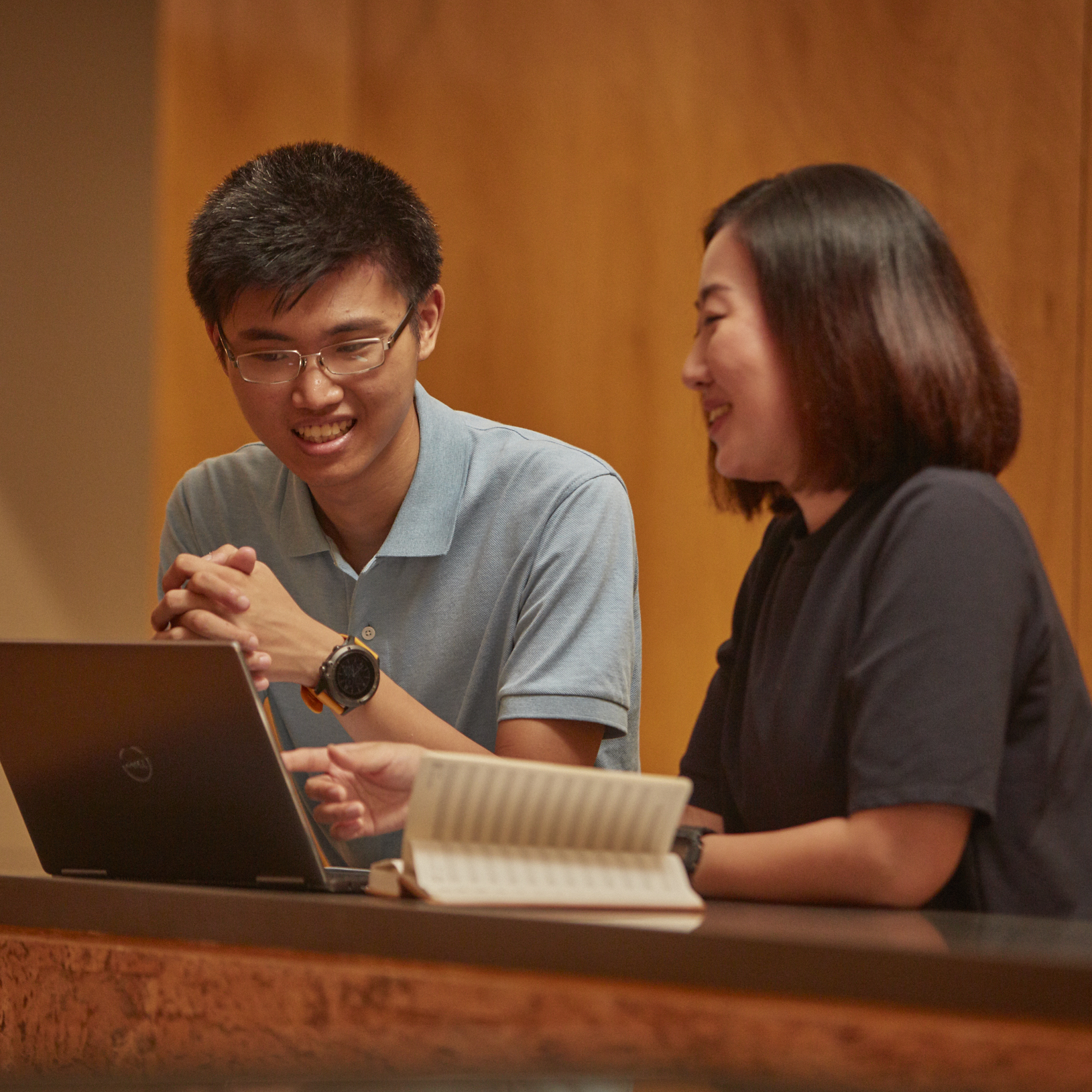 A man and a woman have a conversation in front of a laptop and a notebook.