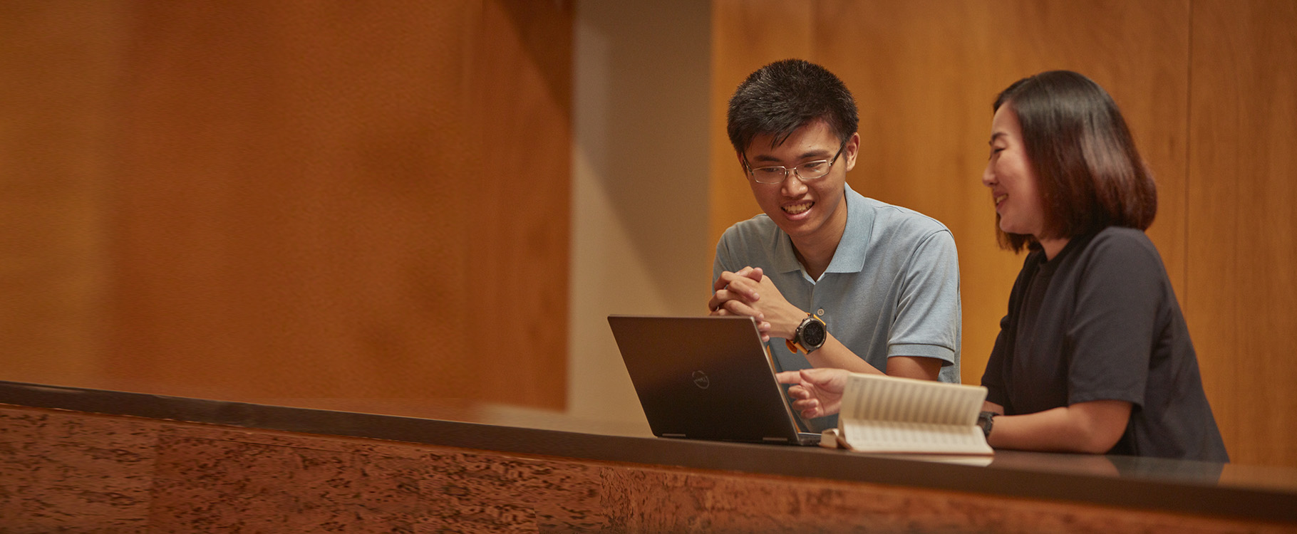 A man and a woman have a conversation in front of a laptop and a notebook.