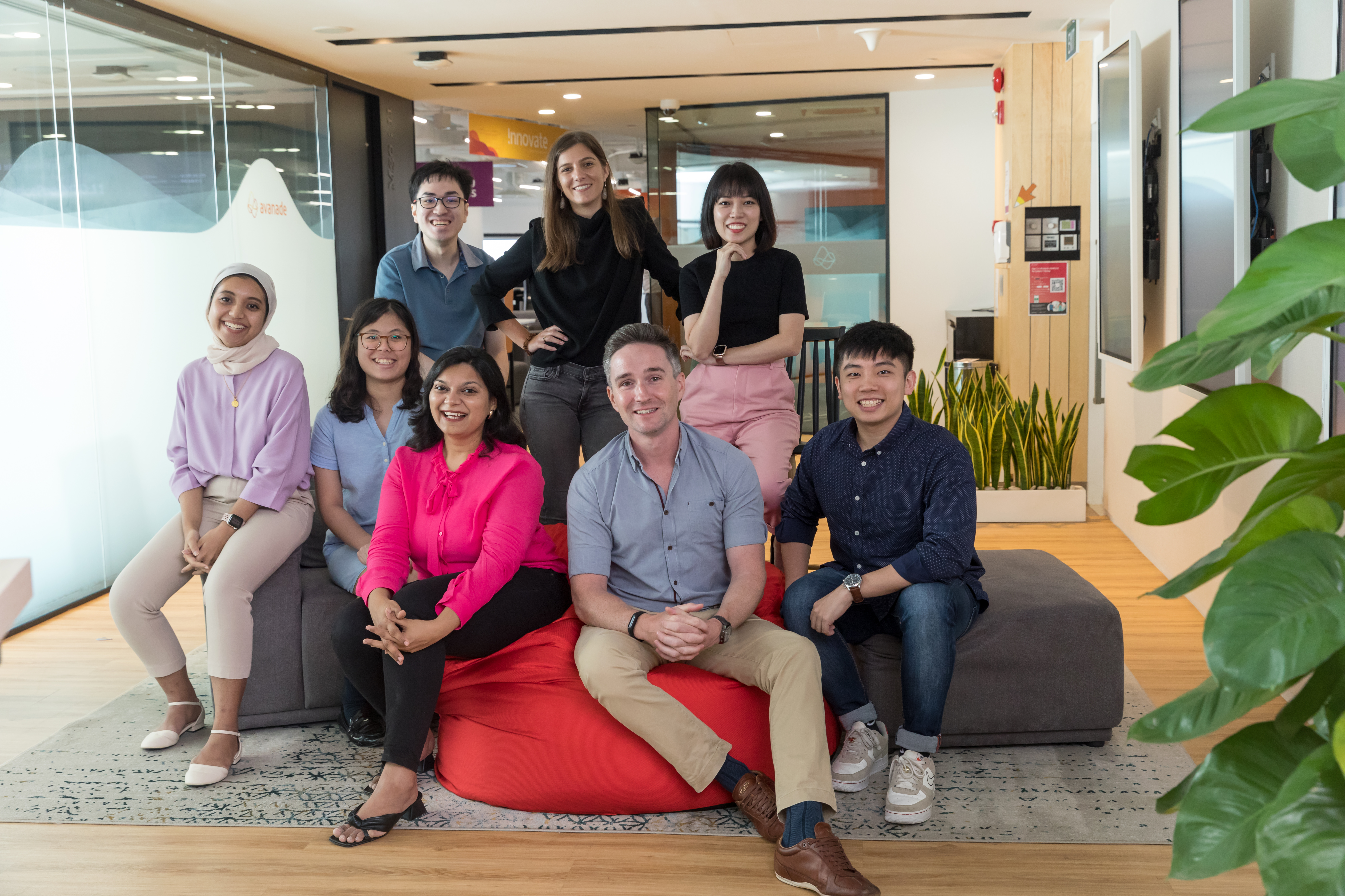 A group of employees pose for the camera while seated on bean bags and couches.