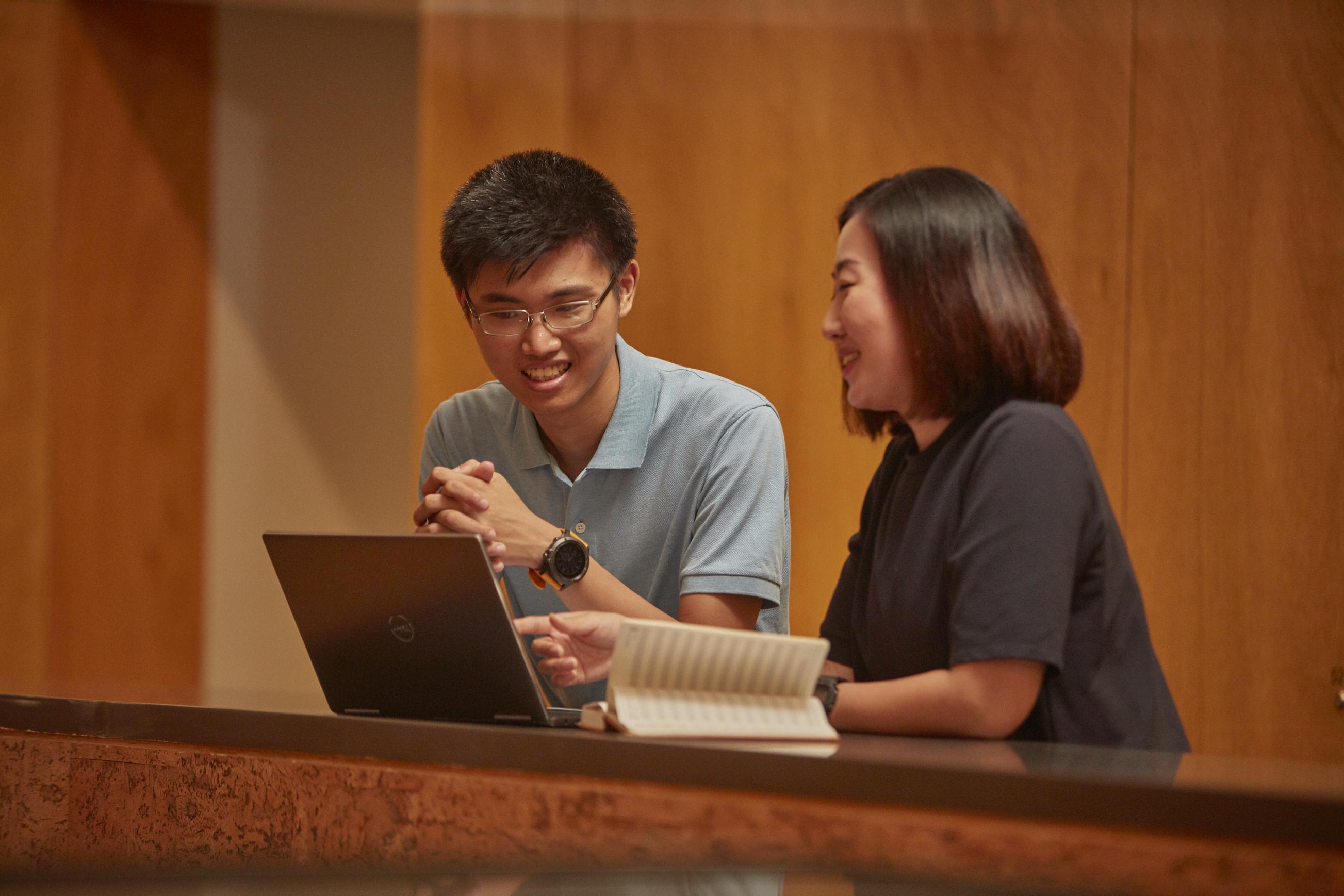 A man and a woman have a conversation in front of a laptop and a notebook.