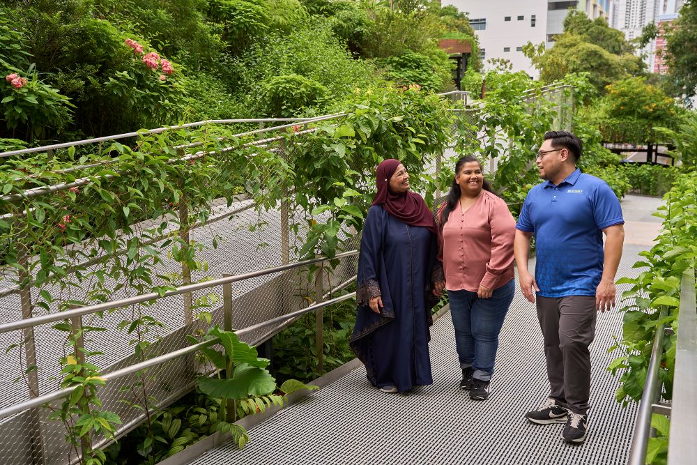 A caregiver with her child with disability walking alongside an SG Enable staff in a garden.