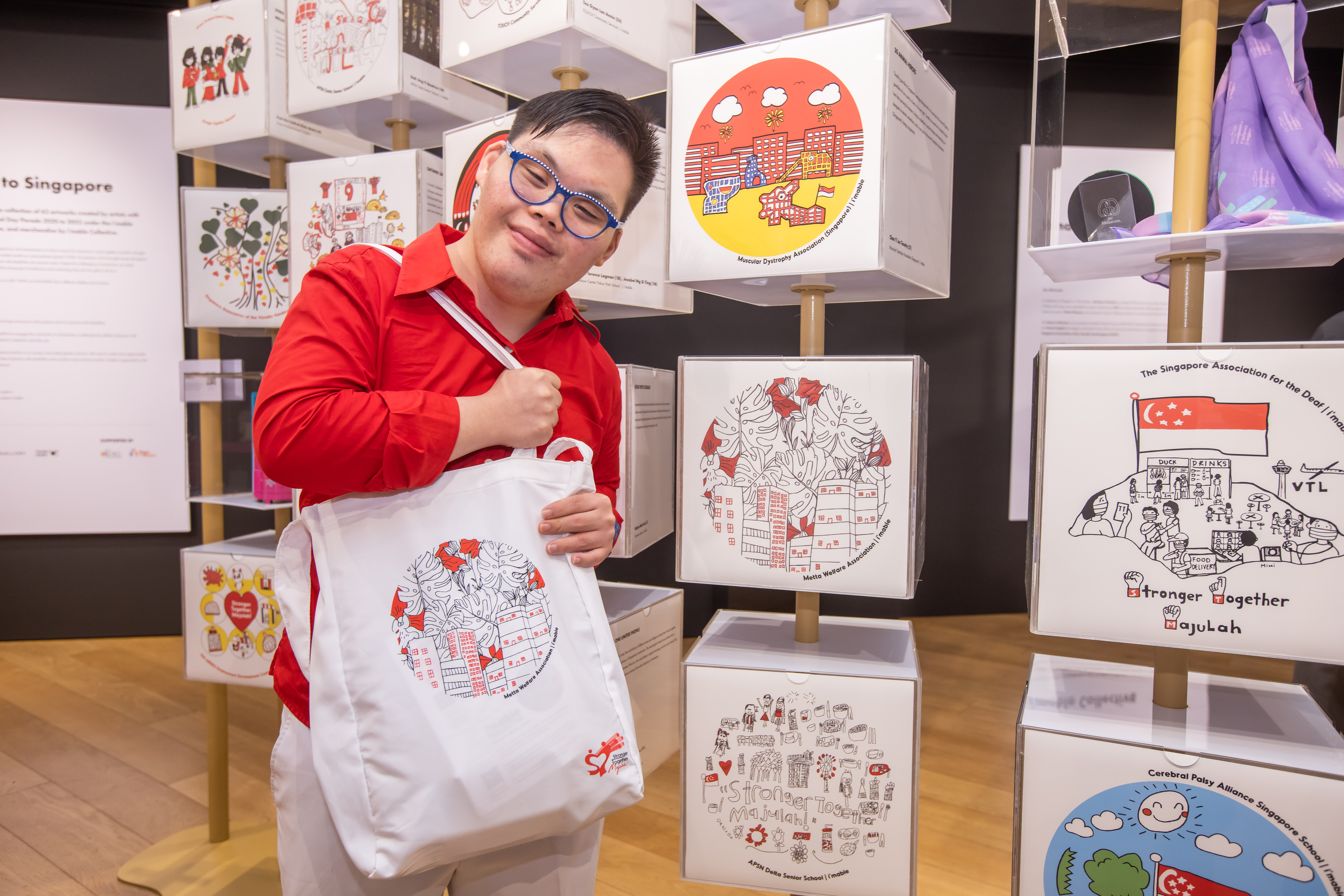 A man dressed in red and white holding an NDP pack standing in front of an exhibit of NDP artworks.