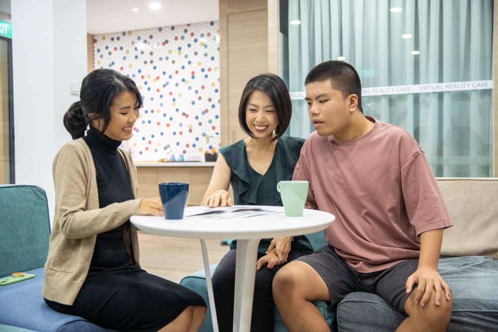 A woman discussing care plans with a mother and her child with disability at a round table.