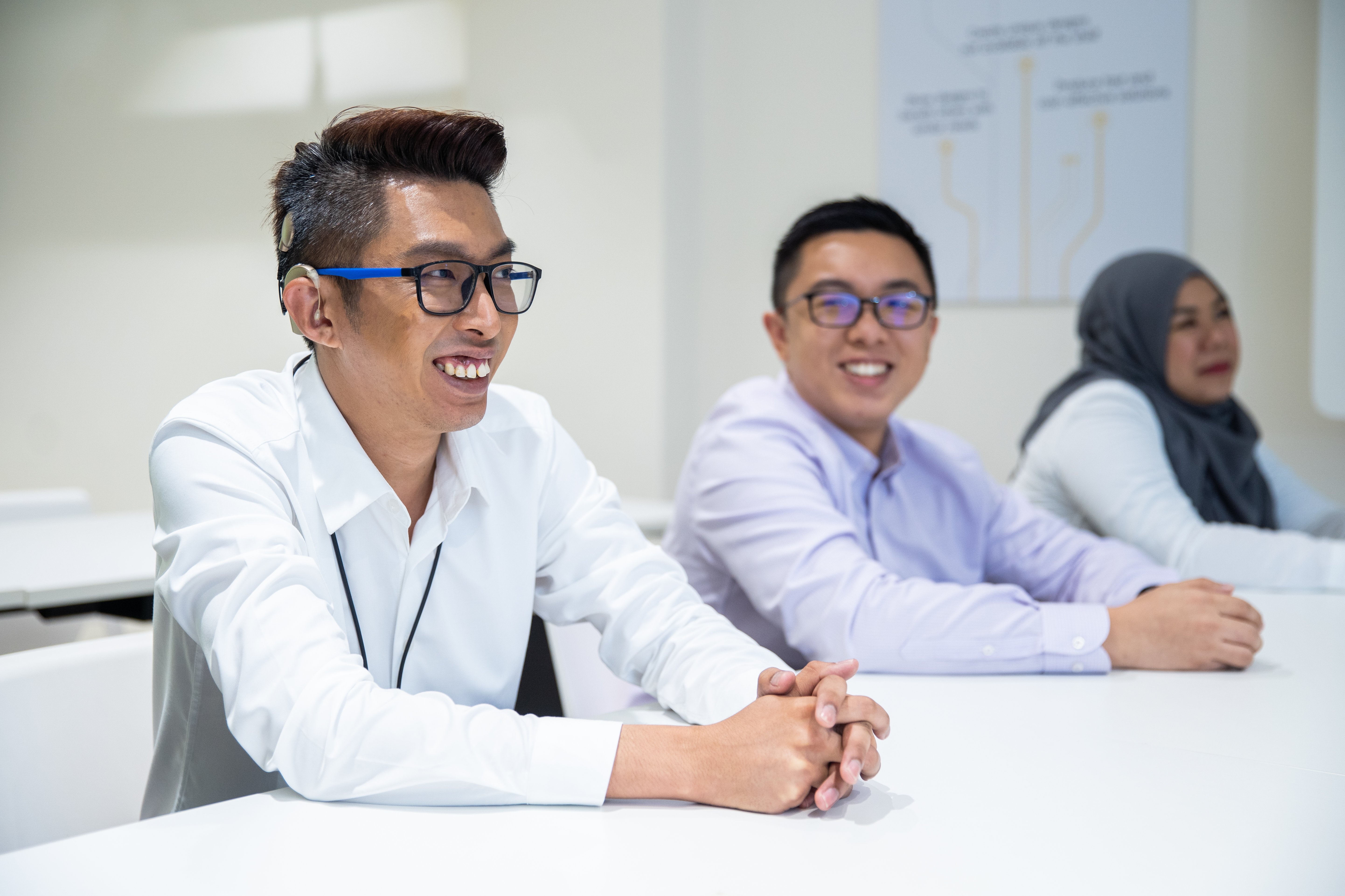 A smiling, bespectacled man wearing a hearing aid, seated beside two other participants.