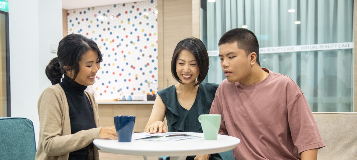 A woman discussing care plans with a mother and her child with disability at a round table.