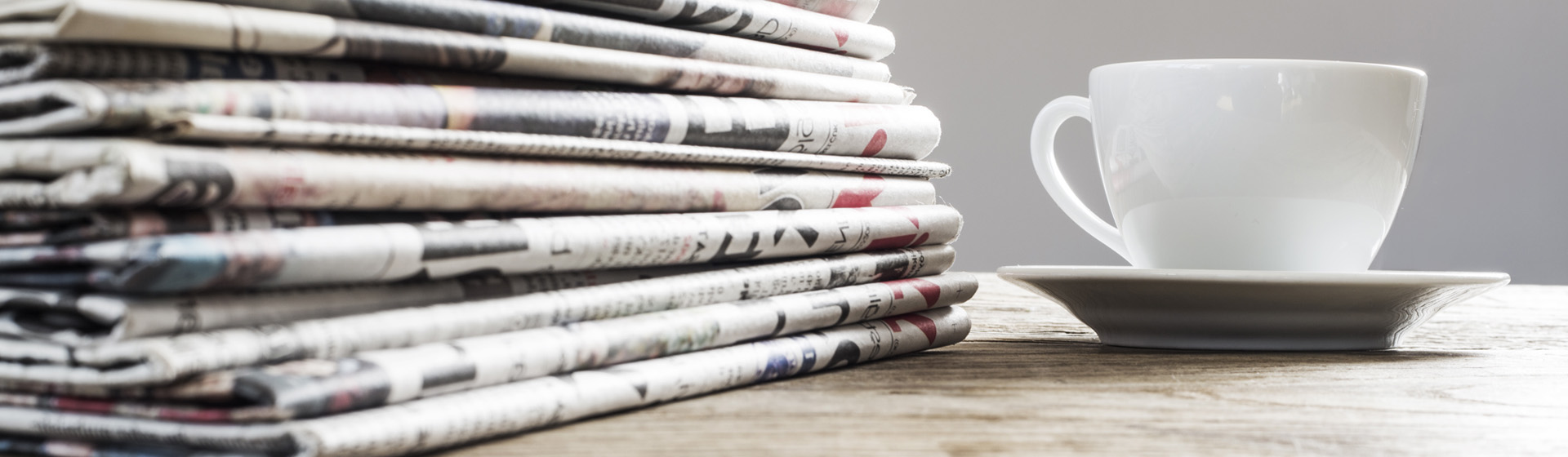 Coffee cup on wooden table next to newspapers