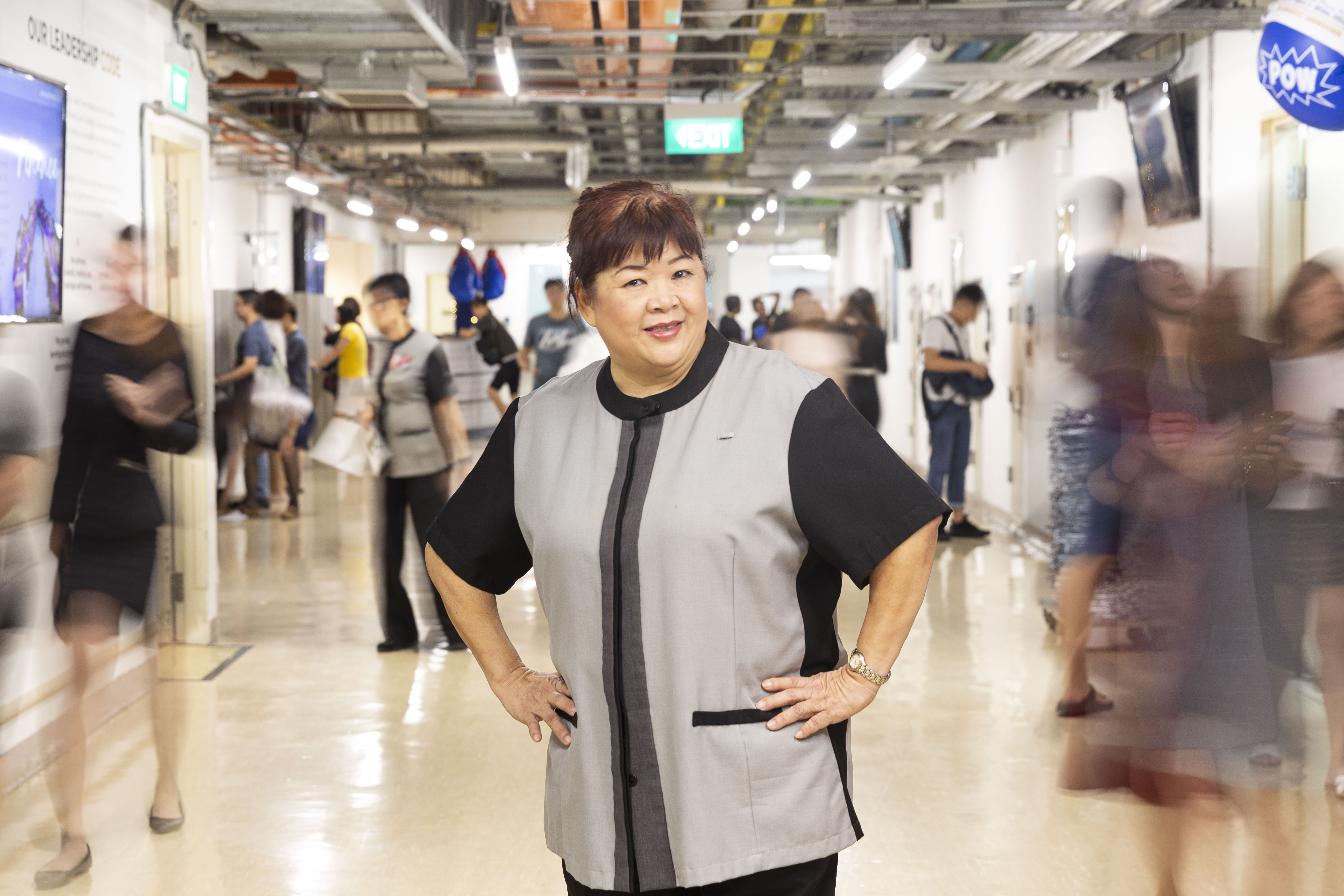 Mdm Lee Poh Tee, Guest Service Agent in the Public Area Department of Marina Bay Sands (MBS), posing in MBS with people moving in the background.