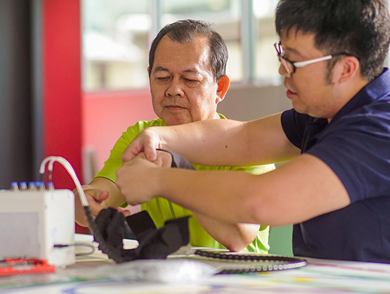A NUS researcher putting on the robotic glove on a stroke survivor to test it out.