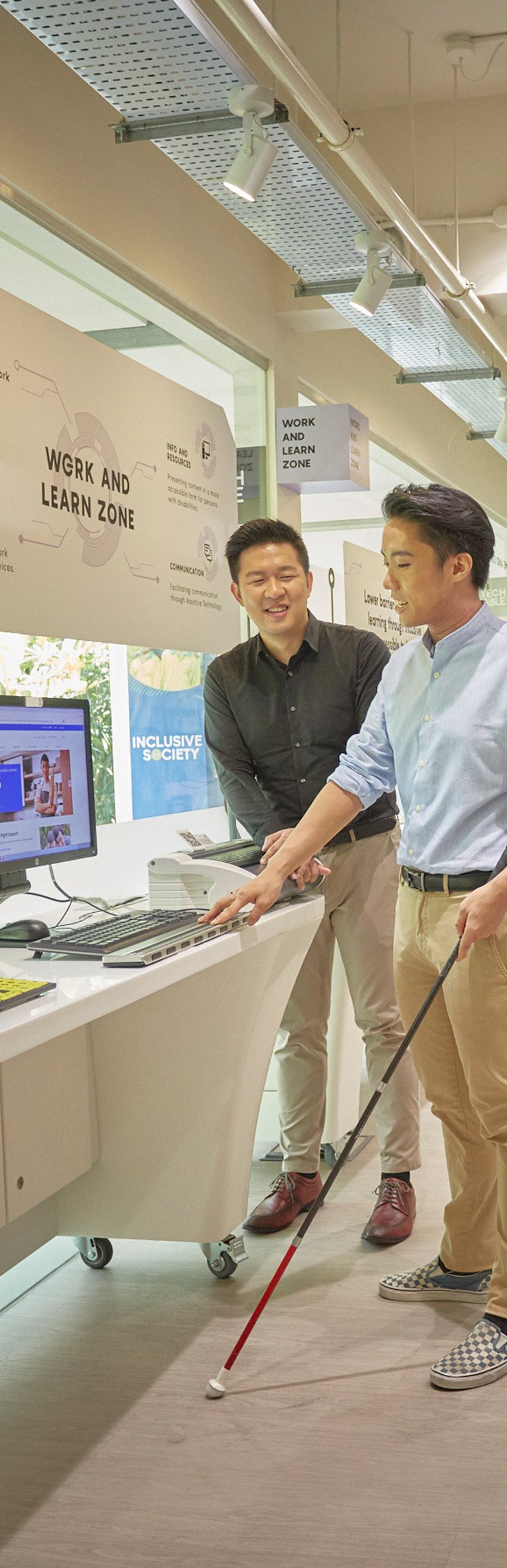 A man is seen guiding a visually impaired man to a braille device at Tech Able.