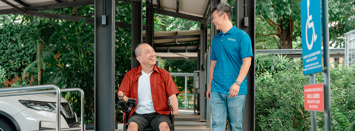 Photo of a man walking with another man in a wheelchair, showing him the way.