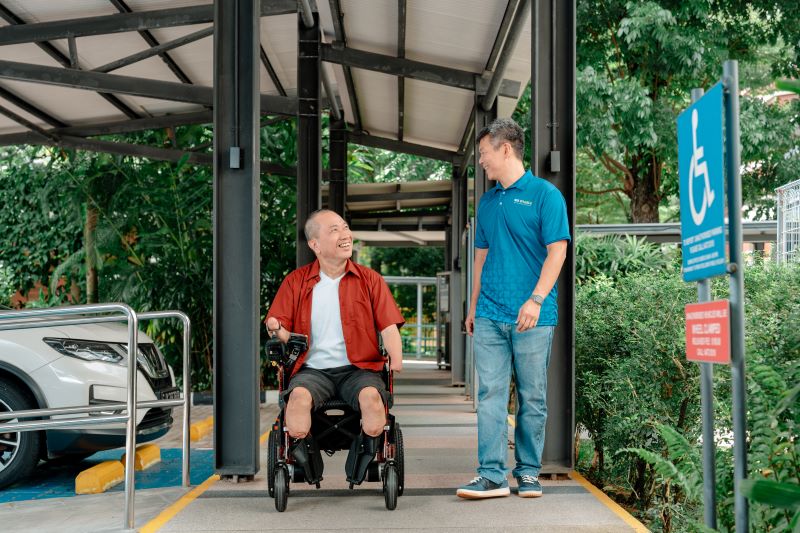 Photo of a man walking alongside another man in wheelchair, showing him the way.