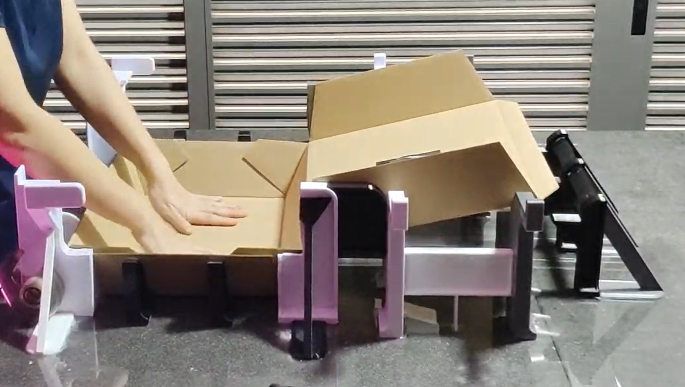 A pair of hands folding cardboard boxes using an assistive tool.