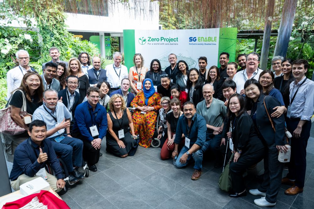 A group of people posing for a photo in Enabling Village, in front of a backdrop with Zero Project and SG Enable logo.